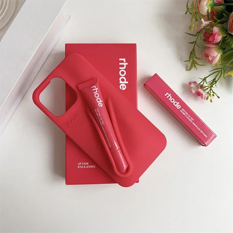 Red 'rhode' lip care products on a white surface with flowers in the corner.