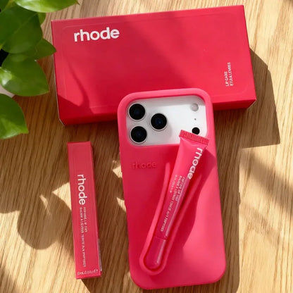 Pink phone case with accessories on a wooden surface, featuring the 'rhode' brand.