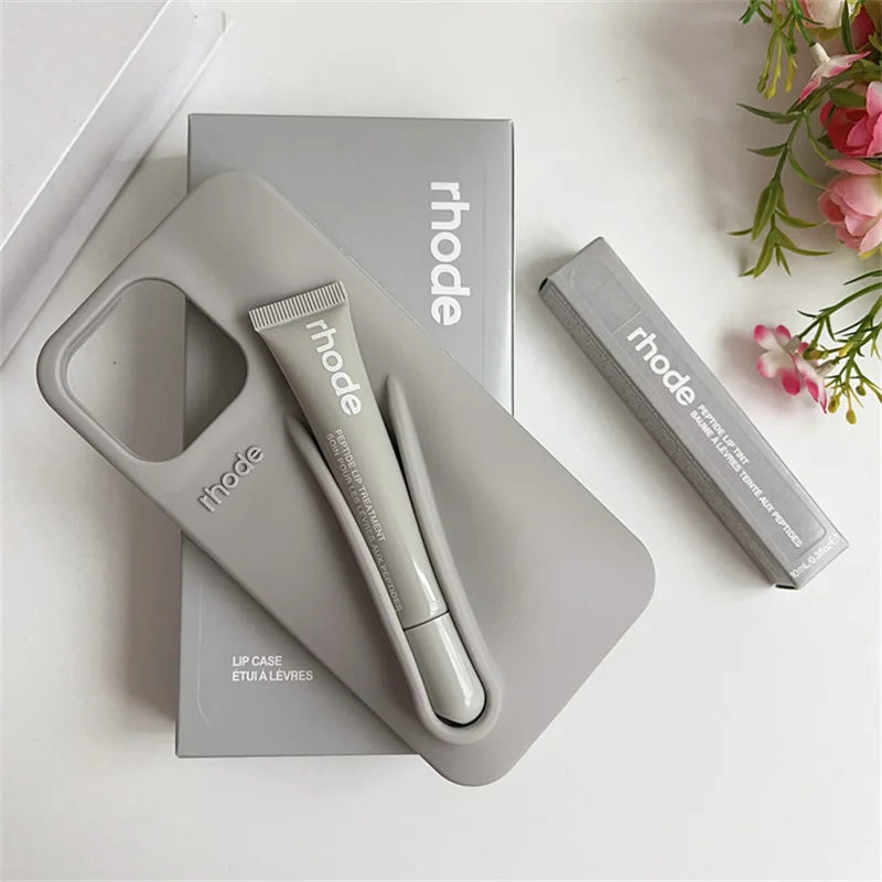 Gray lip case with 'rhode' branding on a white surface with flowers in the corner.