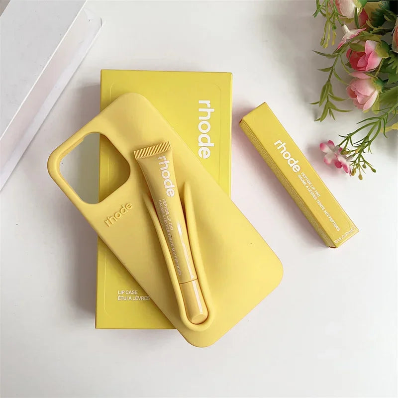 Yellow phone case and stylus set with 'rhode' branding on a white surface with flowers.