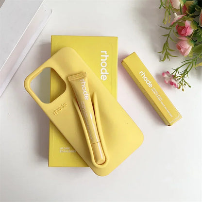 Yellow phone case and stylus set with 'rhode' branding on a white surface with flowers.