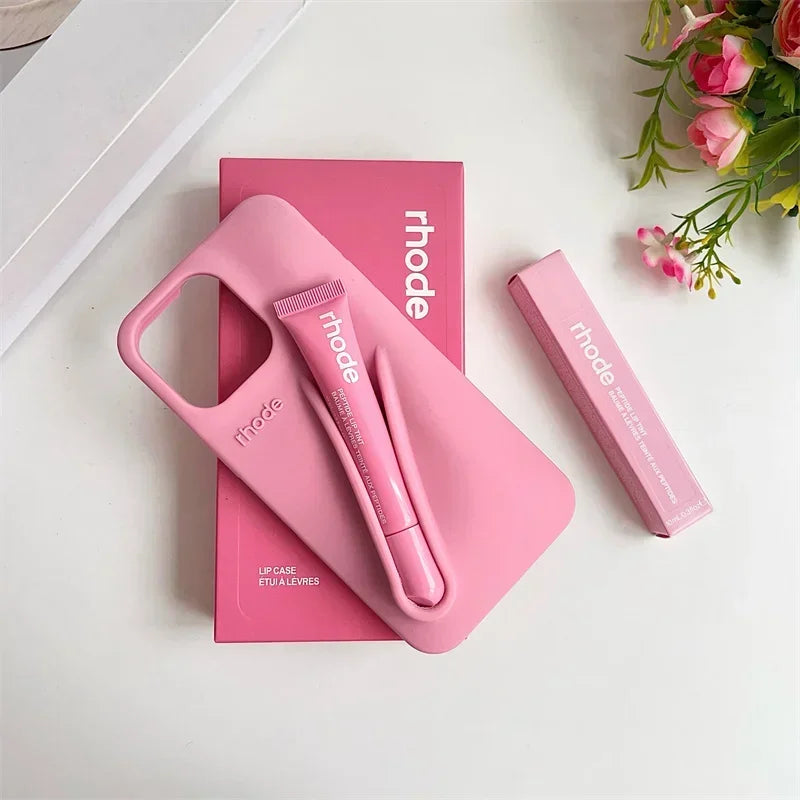 Pink lip care product set with 'rhode' branding on a white surface with flowers.