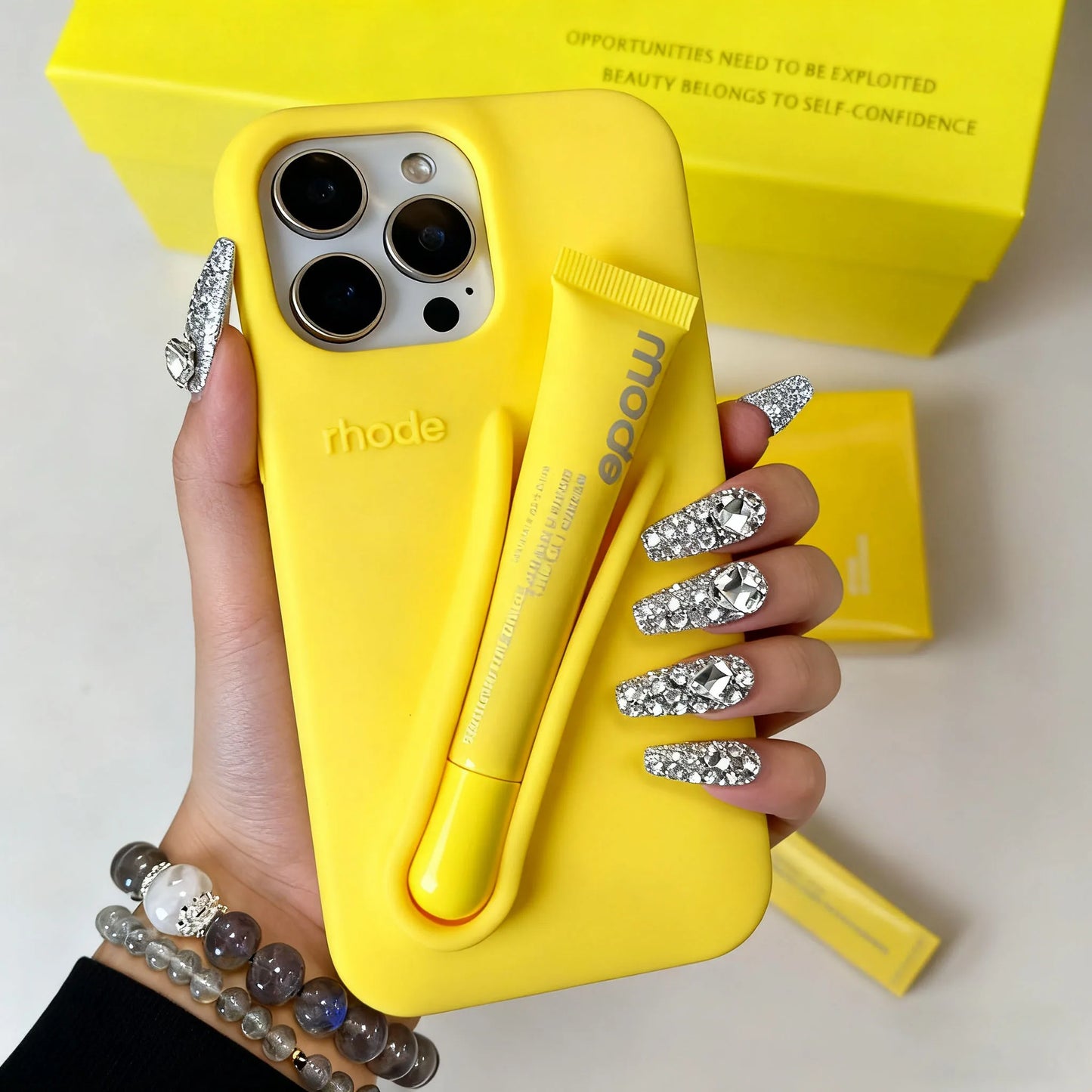 Hand holding a yellow Rhode phone case with 'rhode' branding, against a light background.